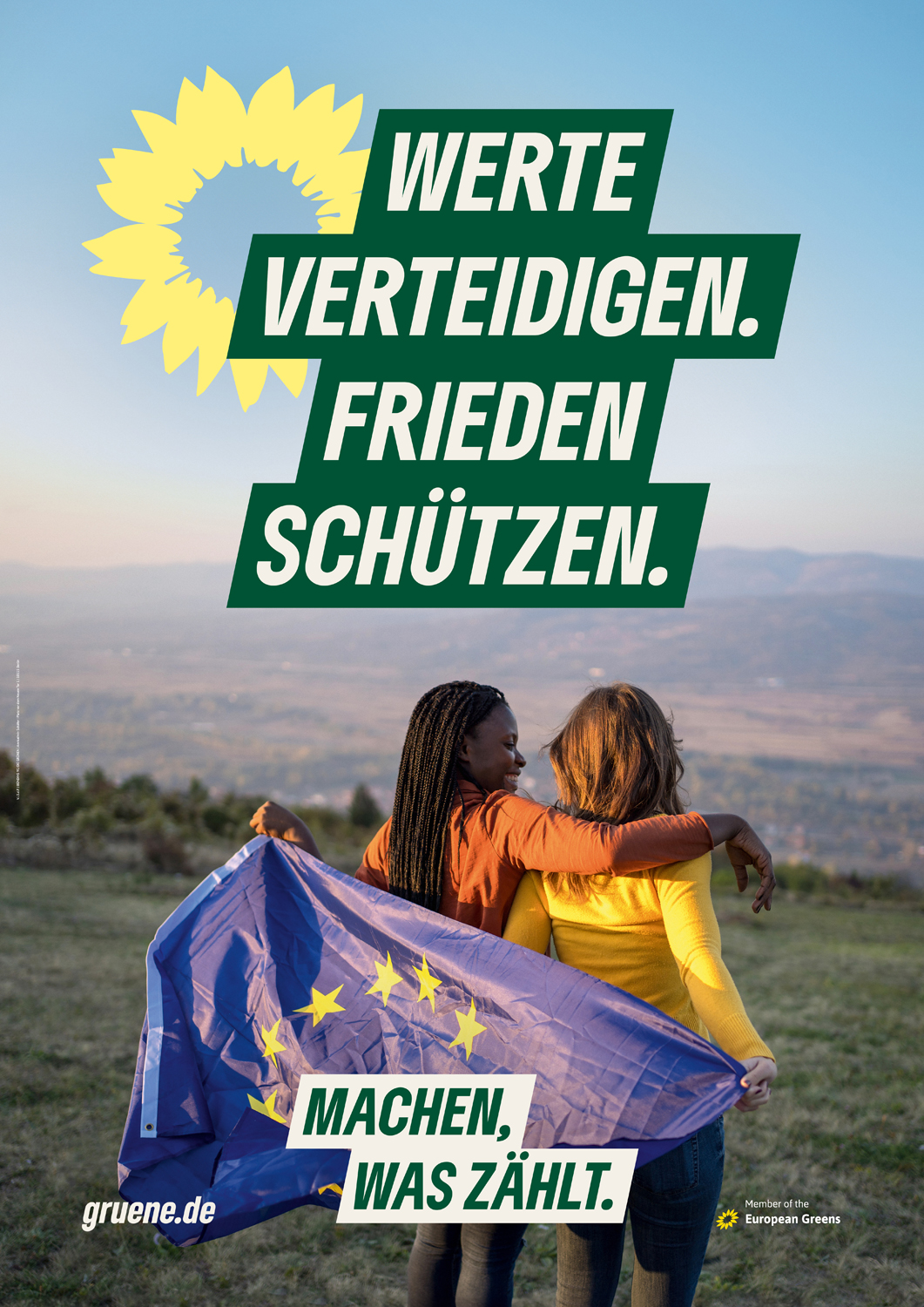 Wahlplakat der Partei Die Grünen zur Europawahl 2024. Es zeigt zwei Menschen, von denen einer den Arm um den anderen legt. Sie haben eine Europafahne über der Schulter. Oben steht groß 'Werte verteidigen, Frieden schützen' und unten 'Machen, was zählt'.